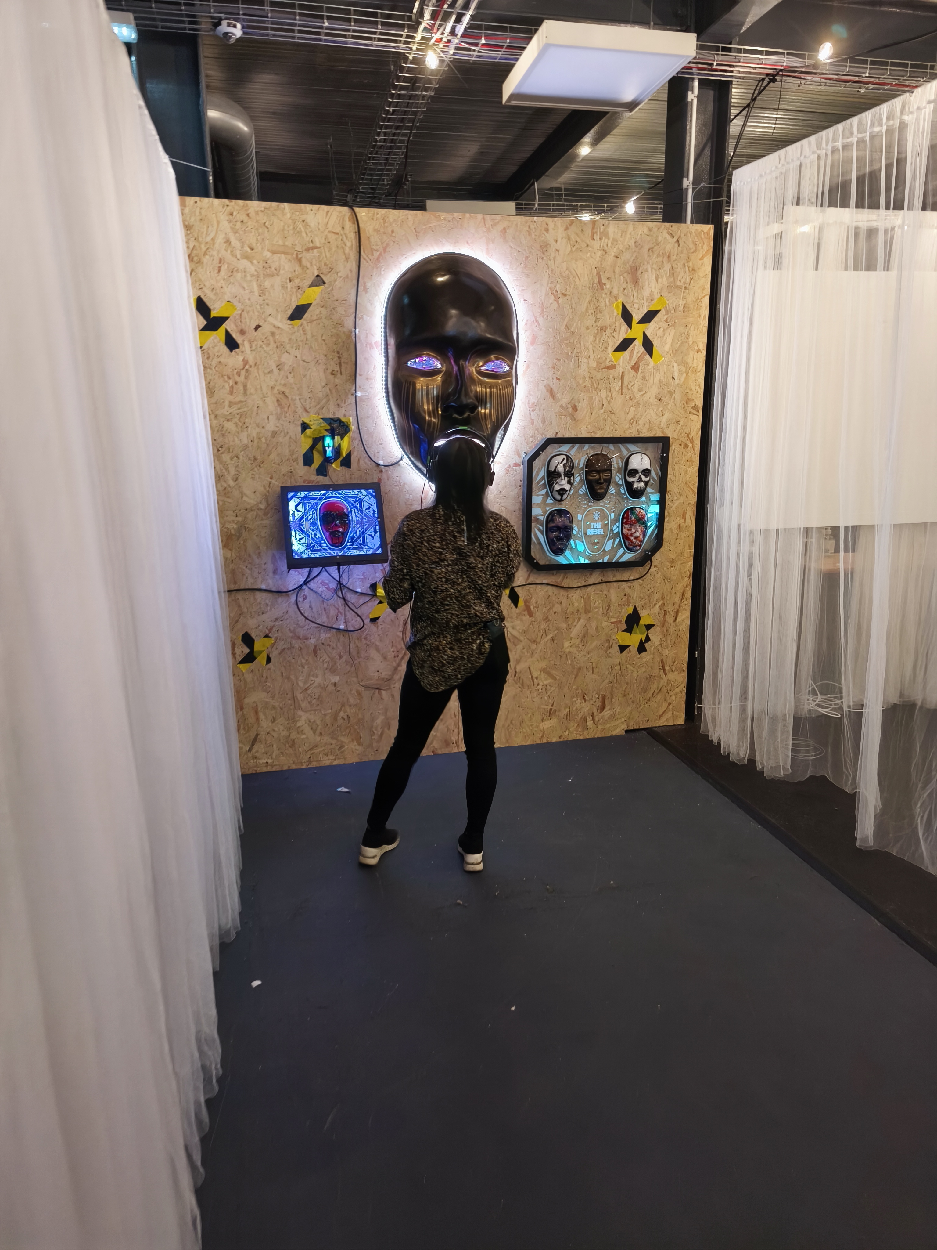 Visitor standing with headphones facing the AILA installation wall