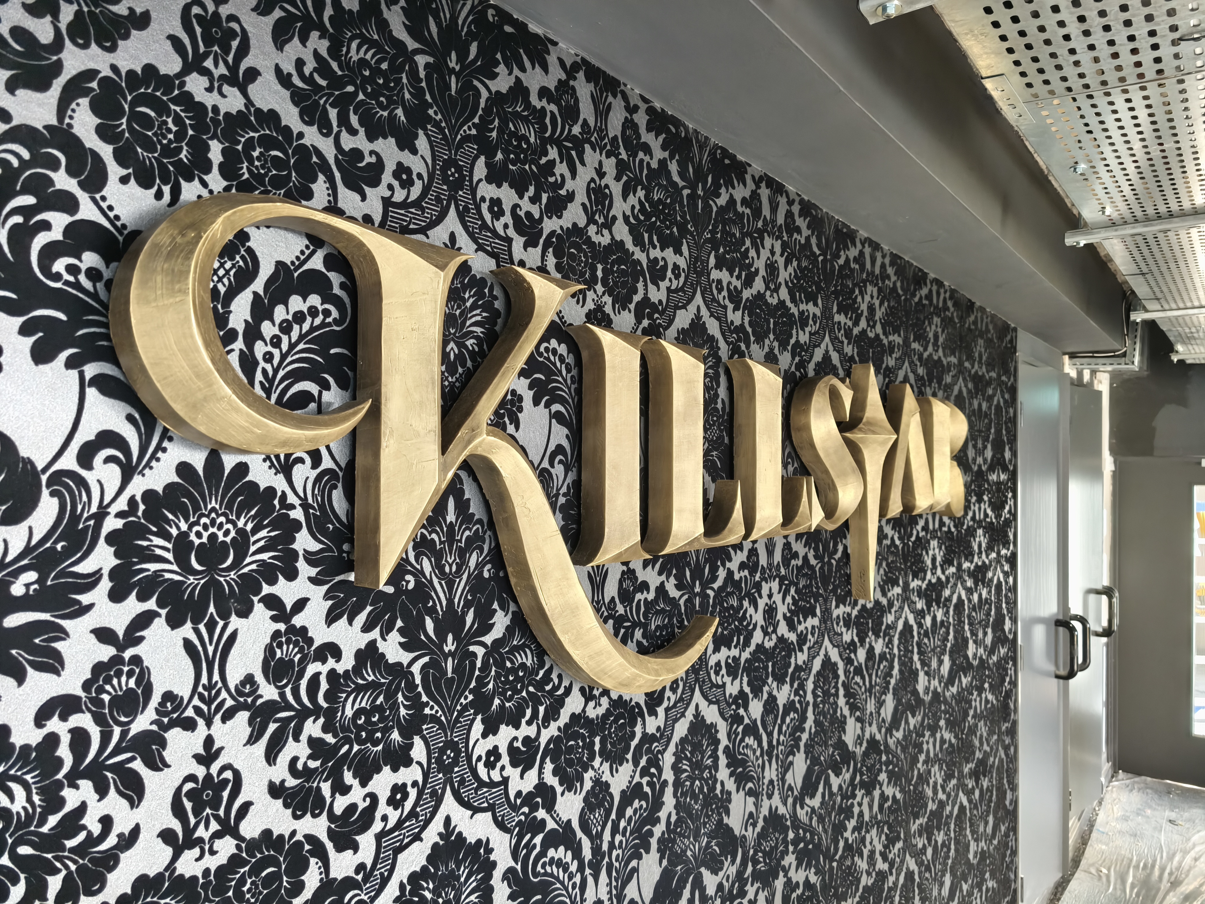 Angled close-up of Killstar lettering from the right, gold finish texture visible