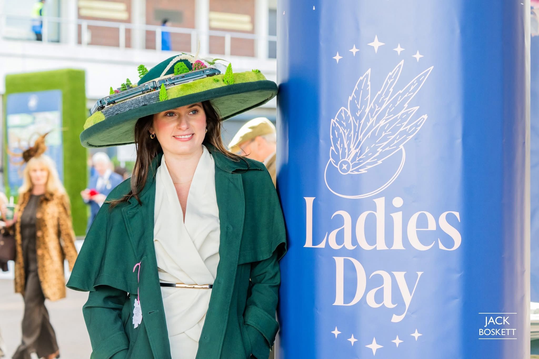 At Cheltenham Racecourse, Ladies' Day banner visible alongside the hat